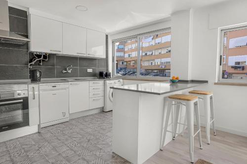uma cozinha branca com um balcão e bancos em Bright Alges Apartment em Algés