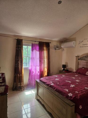 a bedroom with a bed with purple sheets and a window at JA-Spain Retreat in Spanish Town