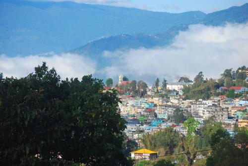 a view of a city in the mountains with clouds at Roots Shoots & Beds in Kalimpong