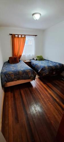 2 Betten in einem Zimmer mit Holzboden in der Unterkunft Casa al lado del Casino in Coihaique
