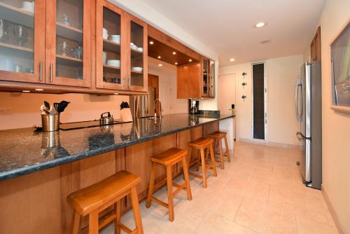 a kitchen with wooden cabinets and bar stools at Maui Kaanapali Villas #D271 in Lahaina
