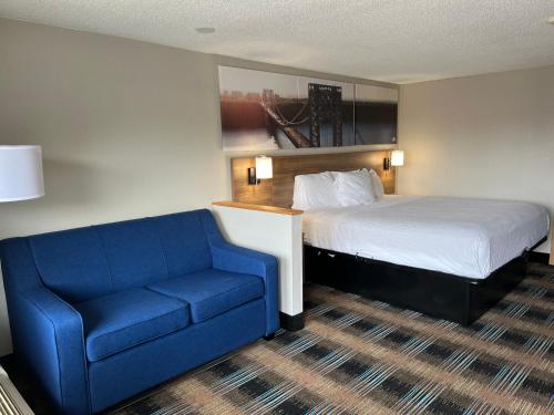 um quarto de hotel com uma cama e um sofá azul em Days-Inn by Wyndham Liverpool-Syracuse em Liverpool