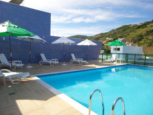 a swimming pool with chairs and umbrellas on a building at Mediterrane Hotel by Castelo Itaipava in Arraial do Cabo