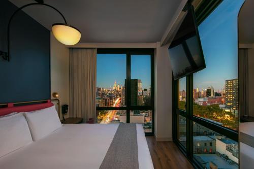 um quarto com uma cama branca e uma grande janela em Moxy NYC Lower East Side em Nova Iorque
