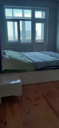 a bed in a room with two windows and a wooden floor at My sweet home in Qara Qarayev in Baku