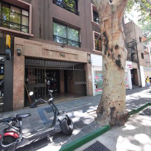 una moto estacionada junto a un árbol frente a un edificio en Departamento Plaza España con cochera en Mendoza