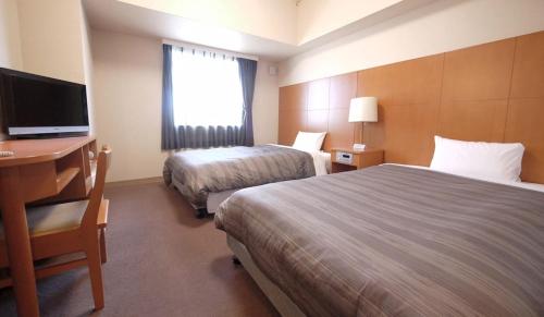 Habitación de hotel con 2 camas, escritorio y TV. en Hotel Route-Inn Shinjyo Ekimae en Shinjo
