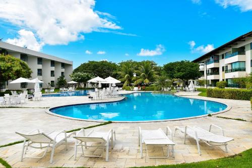 a swimming pool with chairs and tables in front of a building at Carneiros Beach Resort Flat Térreo 2 quartos in Praia dos Carneiros