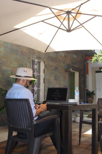 mężczyzna w kapeluszu siedzący przy stole z laptopem w obiekcie Velvet hotel centro histórico w mieście Santa Ana