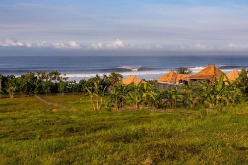 a house in a field with the ocean in the background at Medewi Secret SurfCamp in Pulukan