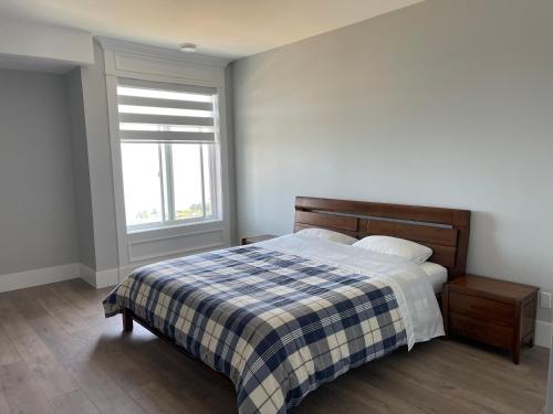 ein Schlafzimmer mit einem Bett mit einer karierten Decke und einem Fenster in der Unterkunft Auspicious Sea View House in Nanaimo