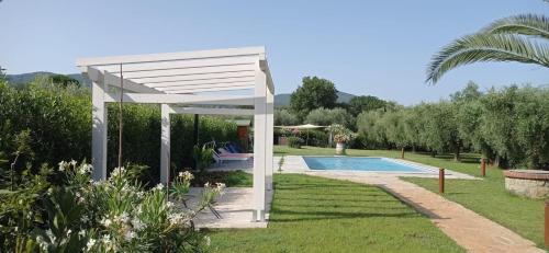a white pergola in a garden with a swimming pool at Appartamenti Gli Ulivi Di Maremma in Gavorrano