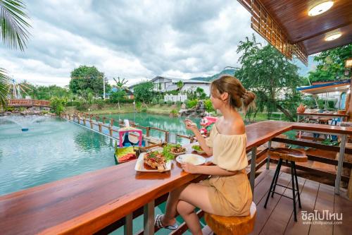 une femme assise à une table avec un repas devant une piscine dans l'établissement ห้างหุ้นส่วนจำกัด บ้านเถ้าแก่, à Ban Muang Baeng
