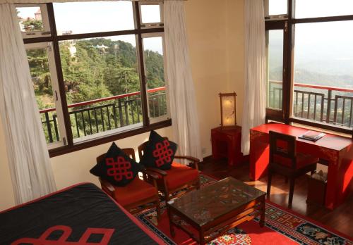 a living room with red chairs and a desk and windows at New Serkong House in Dharamshala