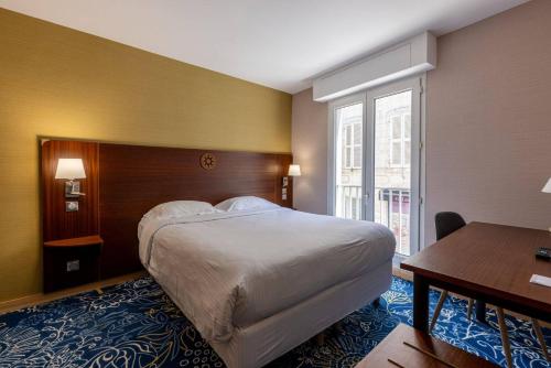 ラ・ロシェルにあるHôtel Le Yachtman, The Originals Collectionの大きなベッドとデスクが備わるホテルルームです。
