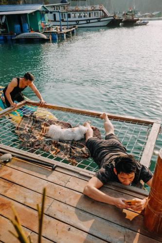 a man laying on a dock next to a net in the water at Lan Ha Floating Homestay in Cat Ba