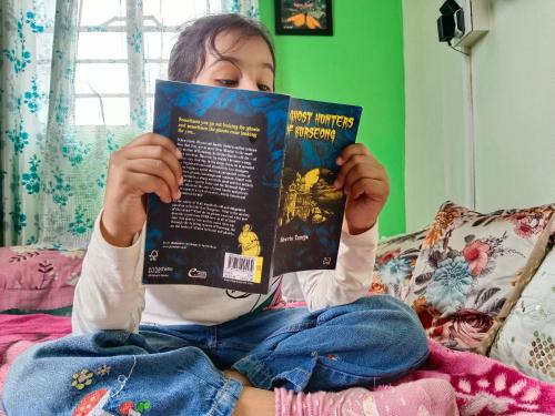 a girl sitting on a bed reading a book at International Youth Hostel and Homestay Kurseong Bazar in Kurseong