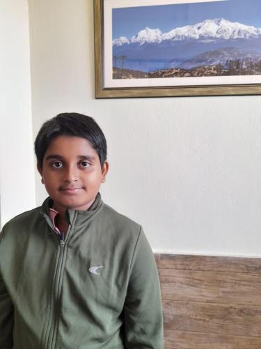 a young boy in a green jacket standing in a room at International Youth Hostel and Homestay Kurseong Bazar in Kurseong