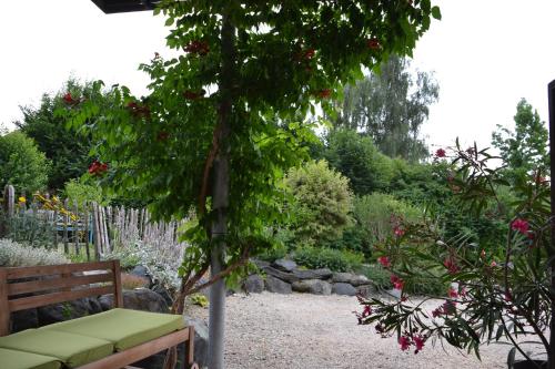 una panchina in un giardino con albero e fiori di Kleine Ferienwohnung für Zwei zwischen Allgäu und Bodensee 
