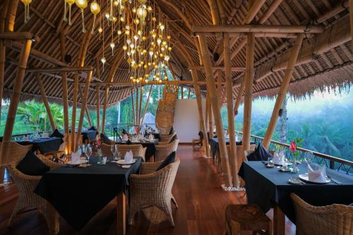 a restaurant with black tables and chairs and chandeliers at Keliki Luxury Lodge in Ubud