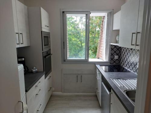 une cuisine avec des placards blancs et une fenêtre dans l'établissement Appartement avec balcon à côté de la plage, à Tourgéville