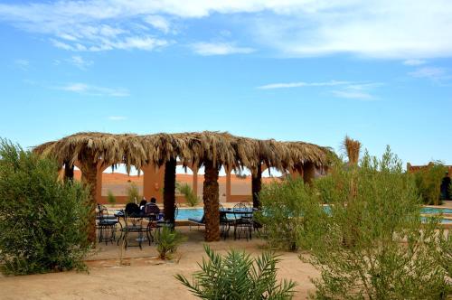 a group of people sitting at a table under a straw umbrella at Kasbah Du Berger & Piscine in Merzouga