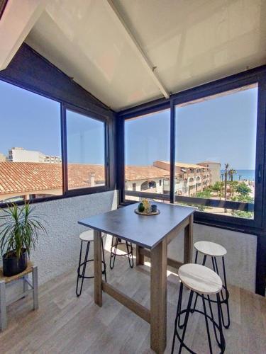 une table et des chaises dans une pièce avec des fenêtres dans l'établissement Appartement Le Barcares avec vue sur mer de type T2 location Arrivée à partir de 15h départ maximum à 11h Location du samedi au samedi juillet et août, au Barcarès