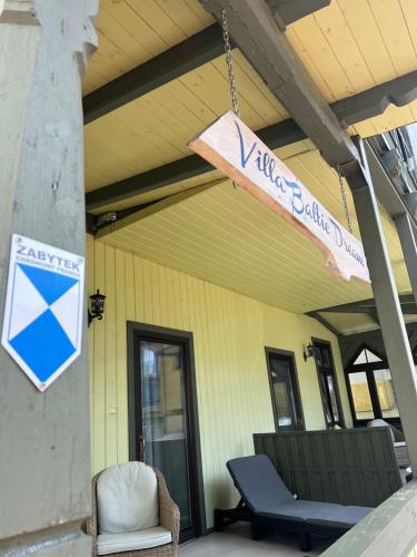 a sign hanging from a porch with a chair and a table at Villa Baltic Dream in Międzyzdroje