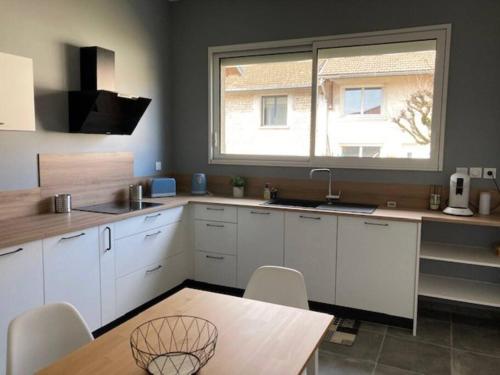 une cuisine avec des armoires blanches, une table et une fenêtre dans l'établissement L’Atelier du Puits Volant, à Meximieux