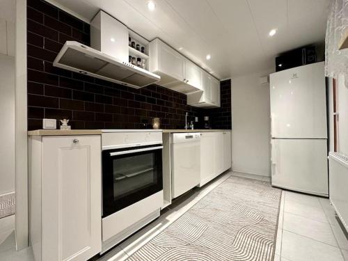 een keuken met witte apparatuur en een zwarte tegelwand bij Nyrenoverat boende i villaområde in Gävle