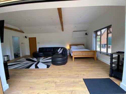 a living room with a black leather couch and a bed at Stansted Airport Luxury Annexe with Parking. in Birchanger