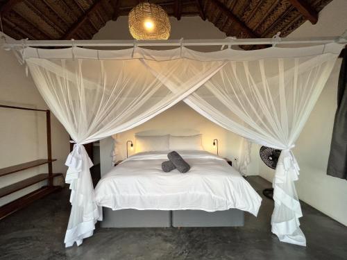 a bedroom with a canopy bed with white curtains at Kumba Lodge in Praia do Tofo