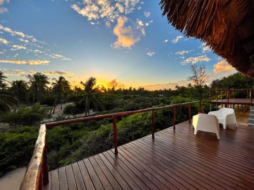 a deck with two white chairs and a sunset at Kumba Lodge in Praia do Tofo