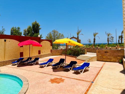 eine Gruppe von Stühlen und Sonnenschirmen neben einem Pool in der Unterkunft Deep Ashri Star House Hotel in Marsa Alam City