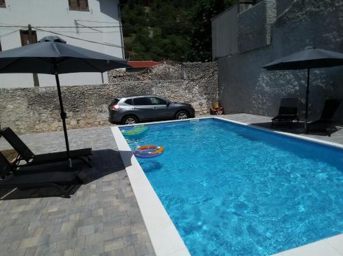 a swimming pool with two umbrellas and a car at Vila Hana in Stolac
