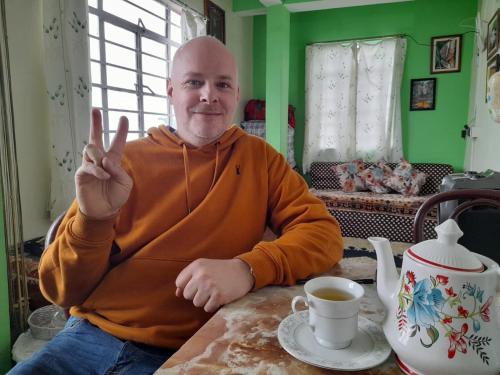 a man sitting at a table with his peace sign at International Youth Hostel and Homestay Kurseong Bazar in Kurseong