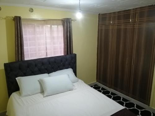 Un dormitorio con una cama con almohadas blancas y una ventana en Mwamba Homes, en Kisii