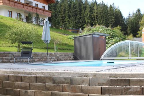 a pool with an umbrella and a chair and a table at Salzburger Dolomitenhof in Annaberg im Lammertal