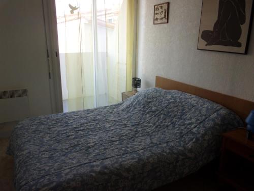 een slaapkamer met een bed met een blauw dekbed en een raam bij appartement saint hilaire de riez 85270 in Saint-Hilaire-de-Riez