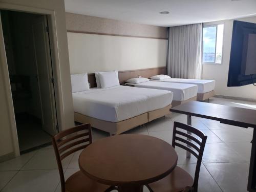 um quarto de hotel com duas camas e uma mesa e cadeiras em Pratti Hotel em Linhares