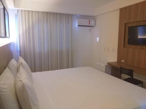 a bedroom with a white bed and a television at Pratti Hotel in Linhares