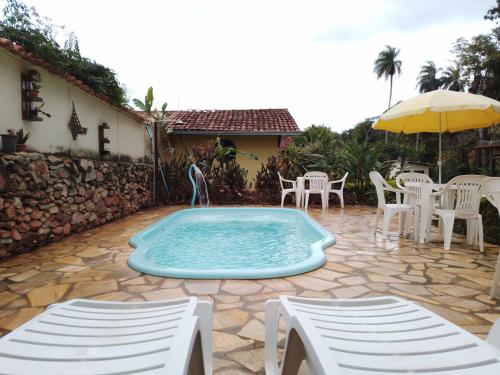 a swimming pool with chairs and a table and an umbrella at Pousada Quintão in Santana do Riacho