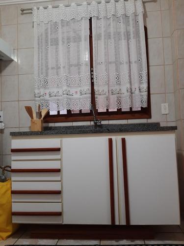 a kitchen counter with a window with white curtains at Apartamento Confortável in Marechal Floriano
