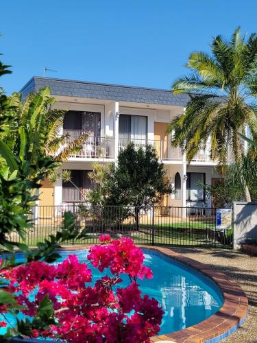 a pool in front of a building with pink flowers at Tower Court Motel - adults only haven in Hervey Bay