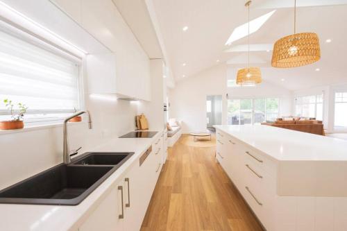 uma cozinha com armários brancos e um lavatório preto em Kiama Family Beach House em Kiama Downs