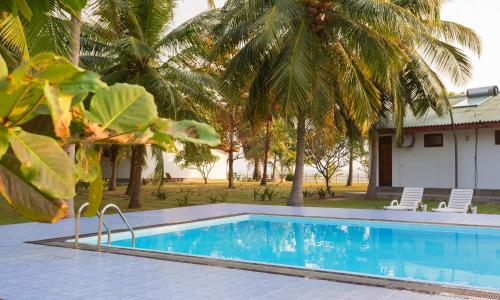 a swimming pool with two chairs and palm trees at Pearl Oceanic Resort - Trincomalee in Trincomalee