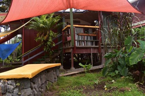 uma casa com um guarda-chuva vermelho e um banco em The Red Cottage and Hawaiian Pond Garden Paradise! em Keaau