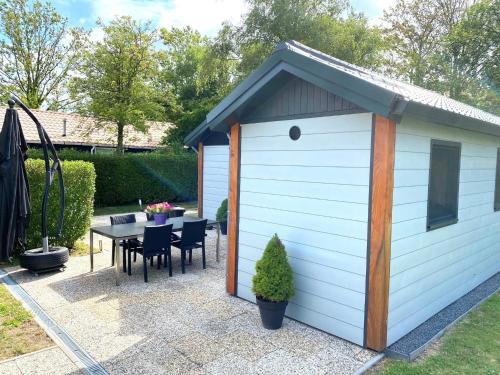 a small white shed with a table and chairs at Oosterschelde Lodge met veel privacy en dicht bij het water in Scherpenisse