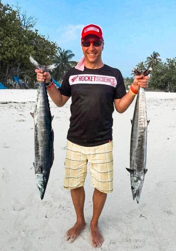 a man holding two fish in his hands on the beach at Tropical Tree in Fehendhoo