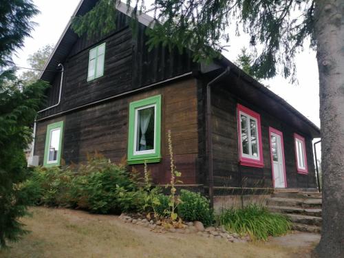 Cette maison en bois est dotée de fenêtres rouges et vertes. dans l'établissement Domek na wsi Wiejsko Czarodziejsko - Agroturystyka Podlasie, 